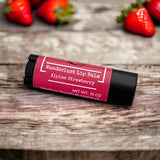 Alpine strawberry lip balm on wooden table with strawberries in background.