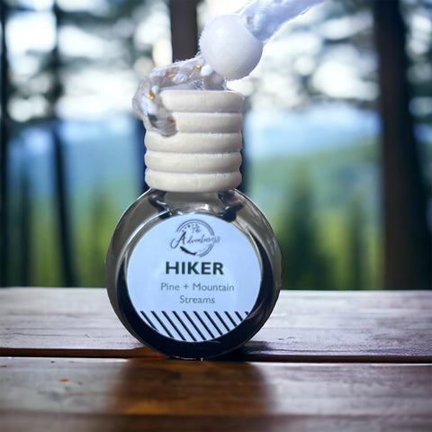 Hiker Car Diffuser sitting on wooden table with pine tree forest in background
