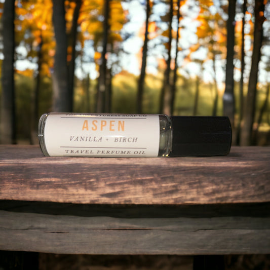 Aspen Perfume Oil laying on wooden table with aspen trees in background.
