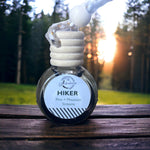 Hiker Car Diffuser sitting on wooden table with sunlit forest in background 