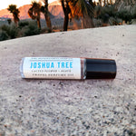 Joshua Tree Perfume Oil with cactus flower and agave laying on rock with joshua trees in background