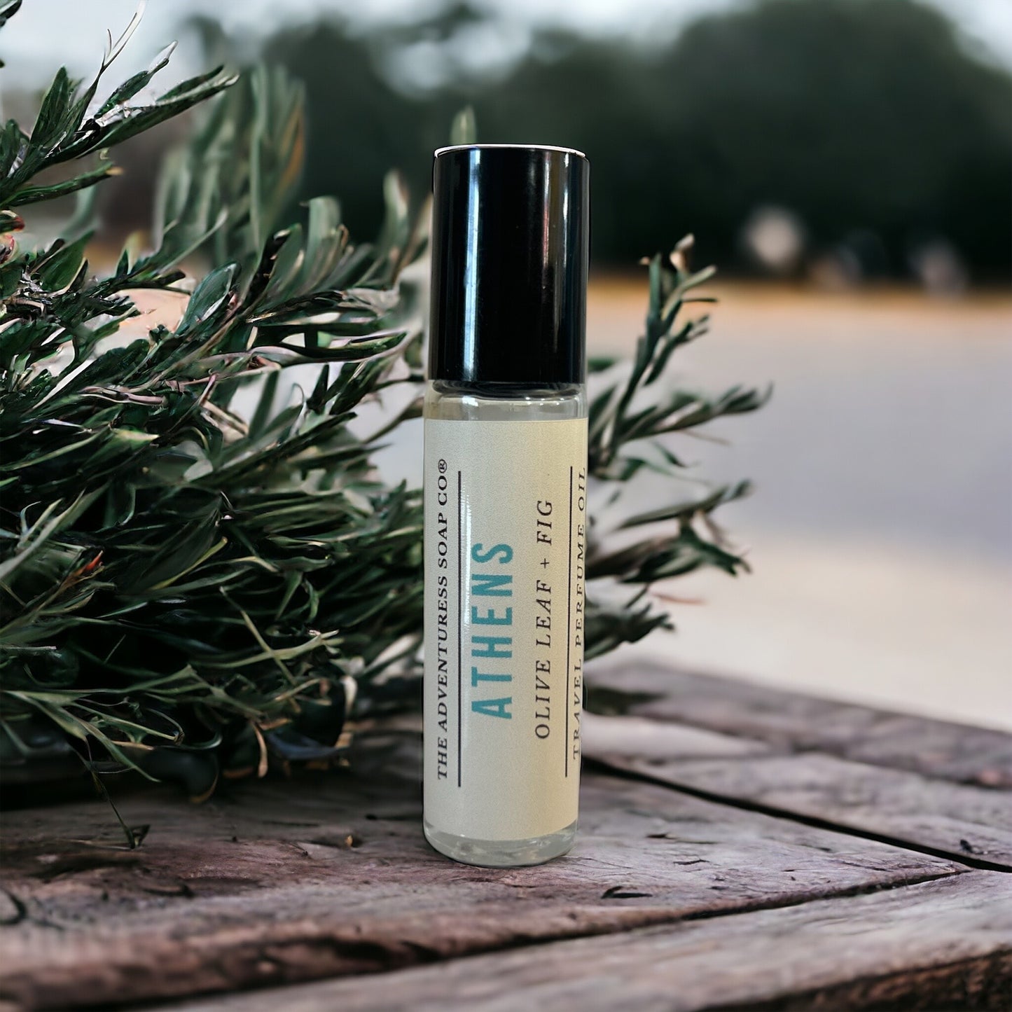 Athens Perfume Oil on wooden table with olive leaf tree.