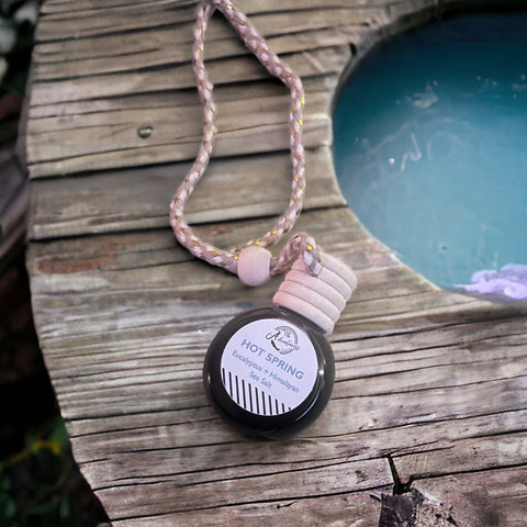 Hot Spring Car Diffuser laying on wooden deck with hot spring in backdrop