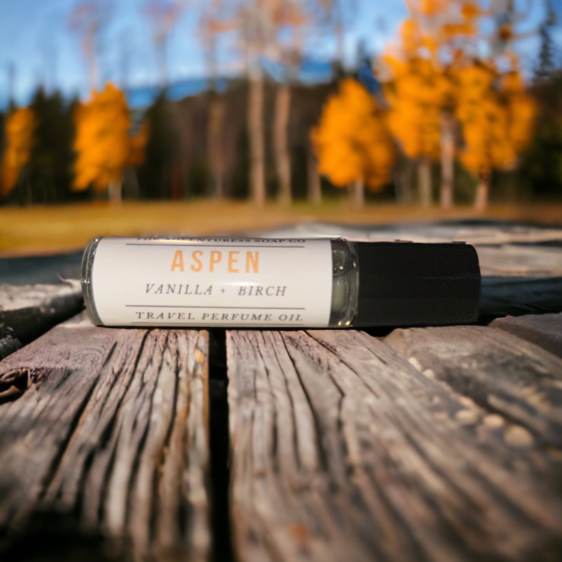 Aspen Perfume Oil laying on wooden table with aspens in background.