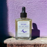Dreamy Bath Body Hair Oil standing in front of lilac colored wall 