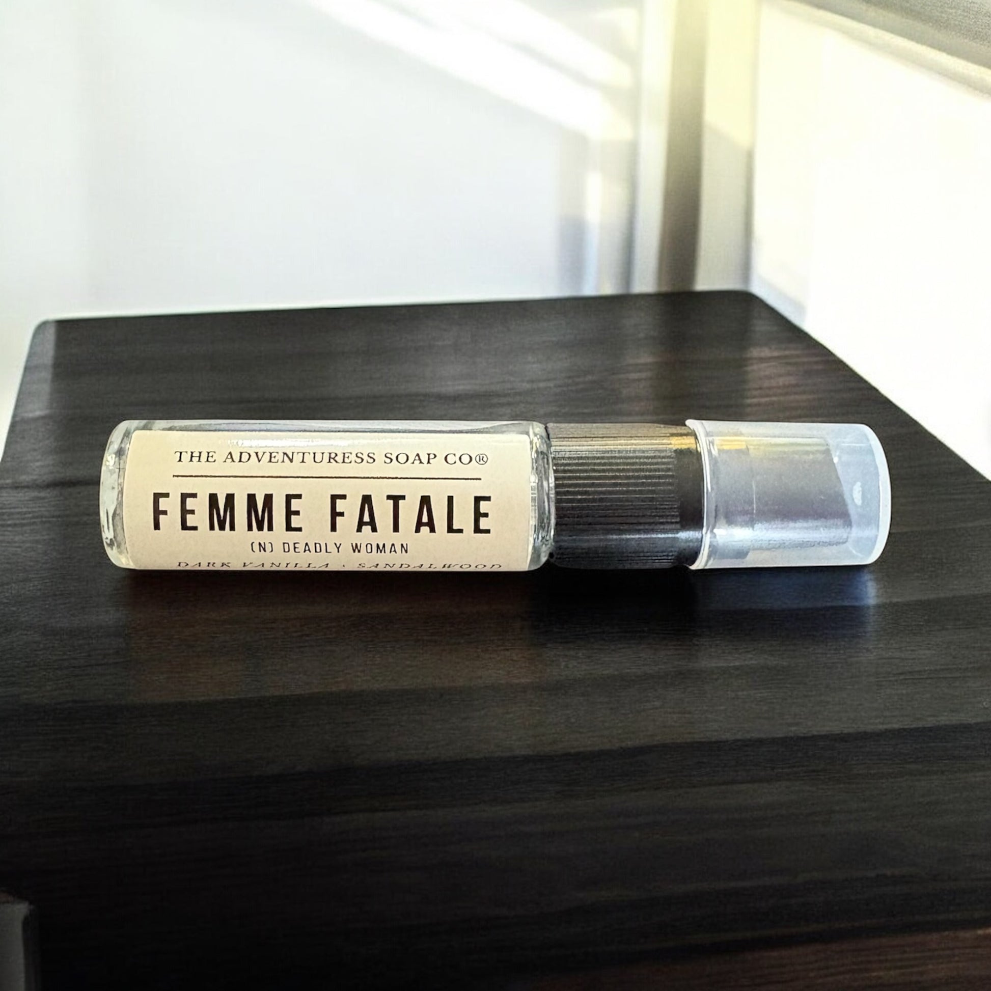 Roll-on bottle labeled 'Femme Fatale' from The Adventuress Soap Co. on a dark wooden surface.