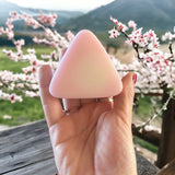 Hand holding small pink mountain shaped soap with cherry blossoms in background