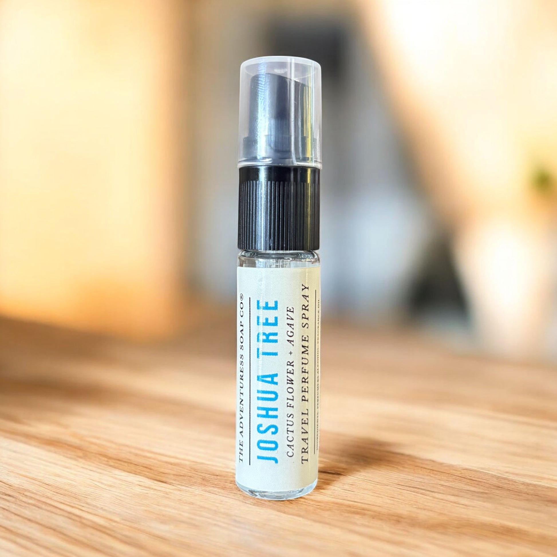 Perfume spray bottle labeled 'Joshua Tree' on a wooden surface with a blurred background