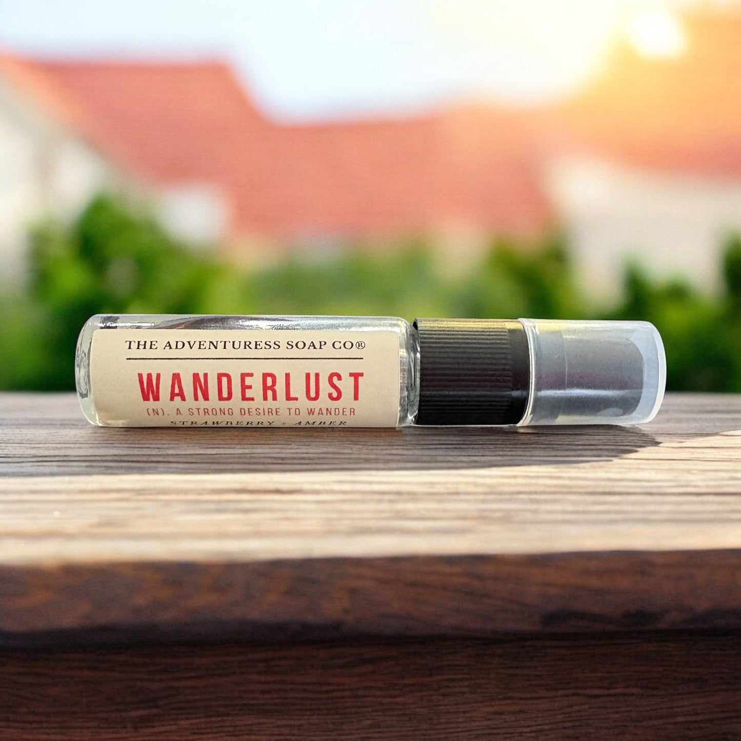 Roll-on bottle labeled 'Wanderlust' by The Adventuress Soap Co. on a wooden surface with a blurred outdoor background.