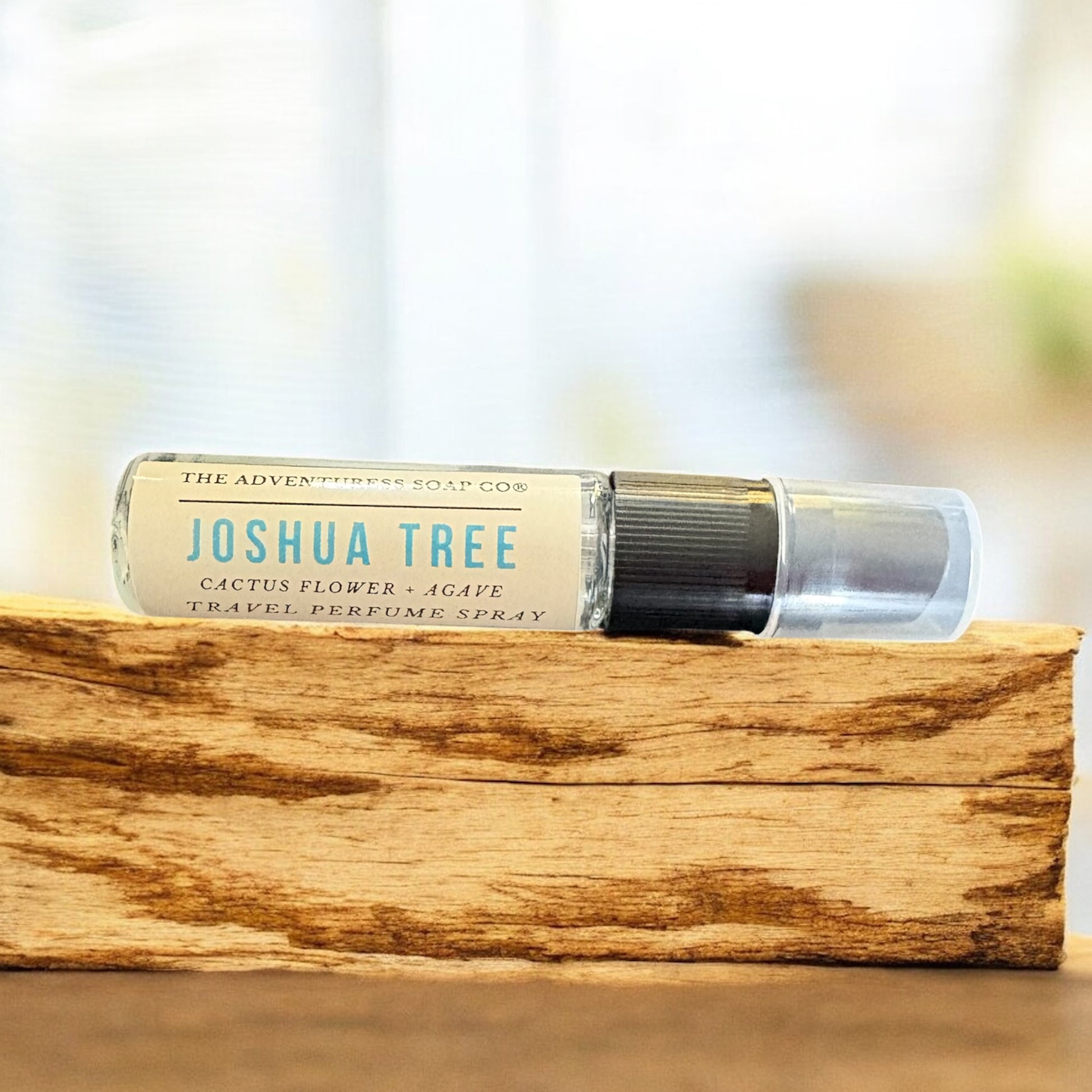 Travel perfume spray bottle labeled 'Joshua Tree' on a wooden surface with a blurred background