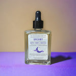 Dreamy Bath Body Hair Oil standing on purple table with yellow background