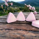 Small pink mountain shaped soaps on wooden table in front of cherry blossoms