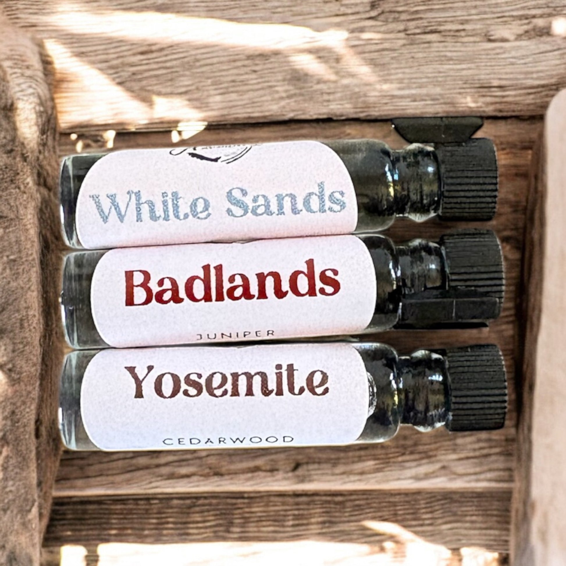 Three small glass bottles with labels 'White Sands', 'Badlands', and 'Yosemite' on a wooden surface.