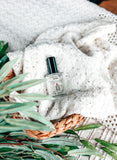 Hygge Eau de Parfum laying on white lacy sheet in basket with green plants
