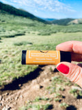 palisade peach lip balm being held with mountains in background