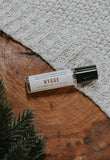hygge perfume oil laying on wood with cozy sweater in background